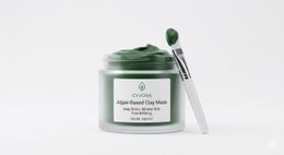 An open jar of dark green Cyvora algae-infused clay mask beside its carton.